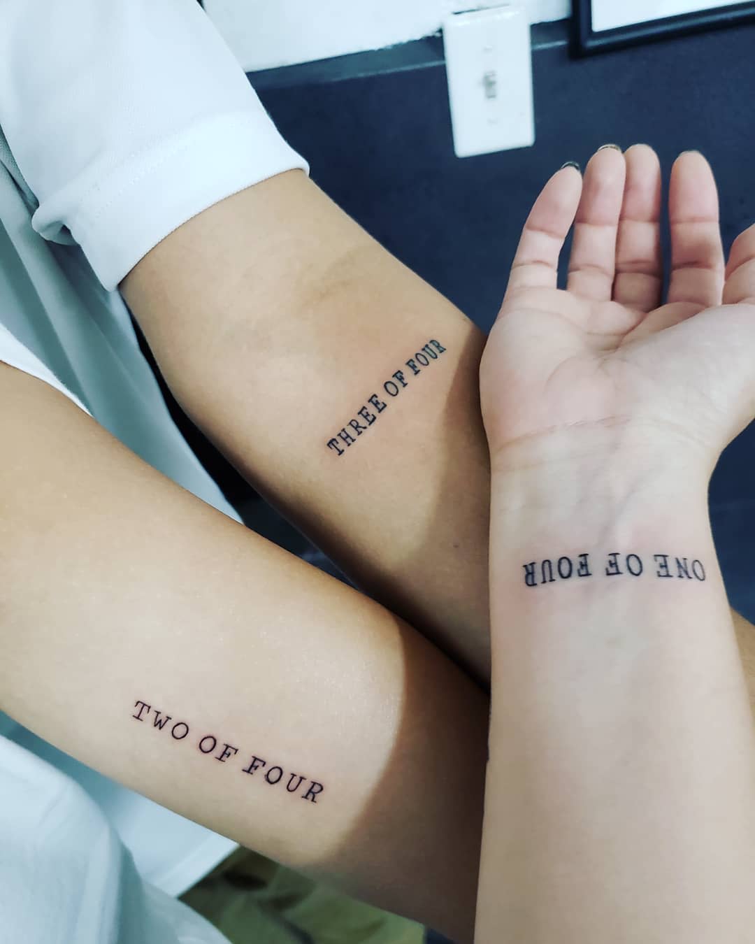 Three tattooed arms with the numbers "ONE OF FOUR," "TWO OF FOUR," and "THREE OF FOUR"